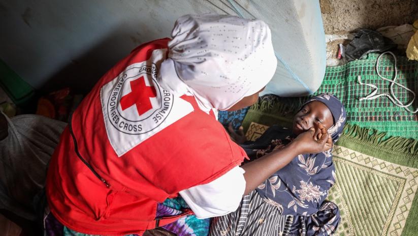 Cameroon Red Cross volunteer, Ramatou, checks a girl's eyes for redness and looks out for other signs and symptoms of measles.